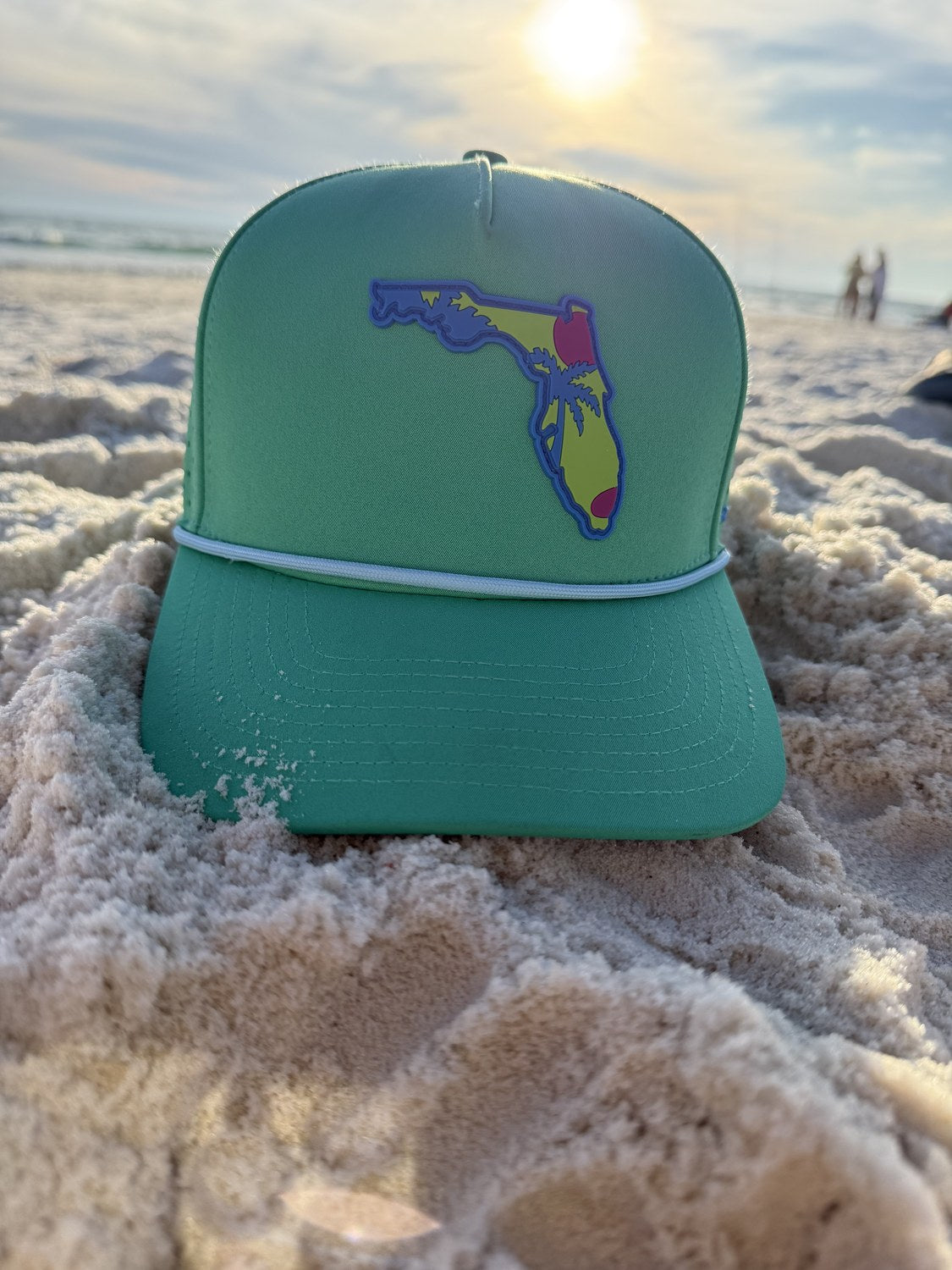 Sunsets and Dinks teal Florida trucker hat on white-sand Panama City Beach at sunset